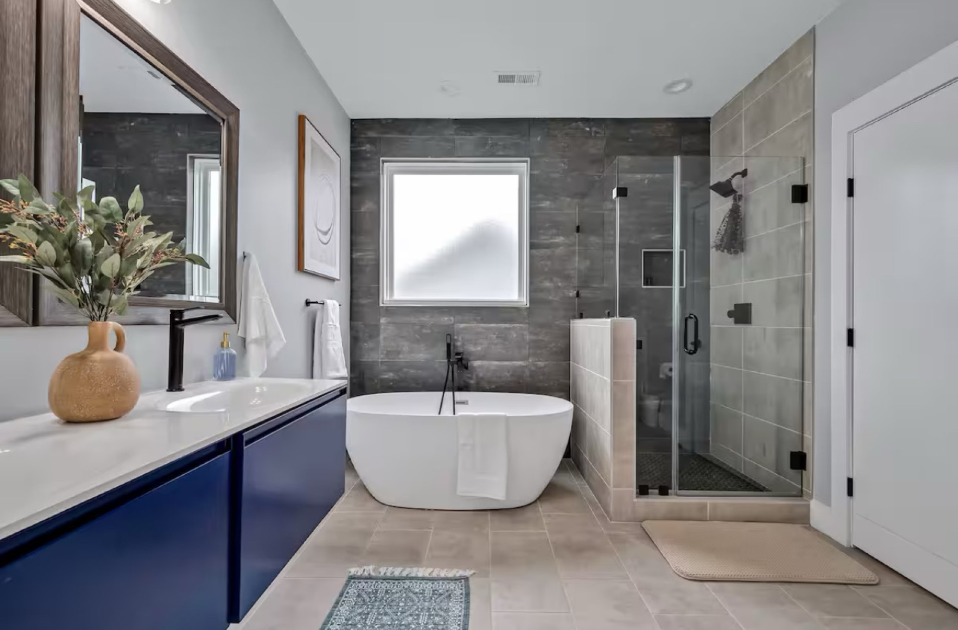 Luxury primary bathroom with navy vanity and freestanding tub renovated by Builder Bee Projects